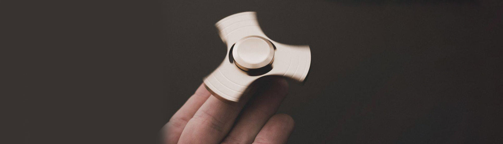 a gold-coloured fidget spinner balanced on a finger while spinning, on a black background-fun fidgets a gold-coloured fidget spinner balanced on a finger while spinning, on a black background-fun fidgets