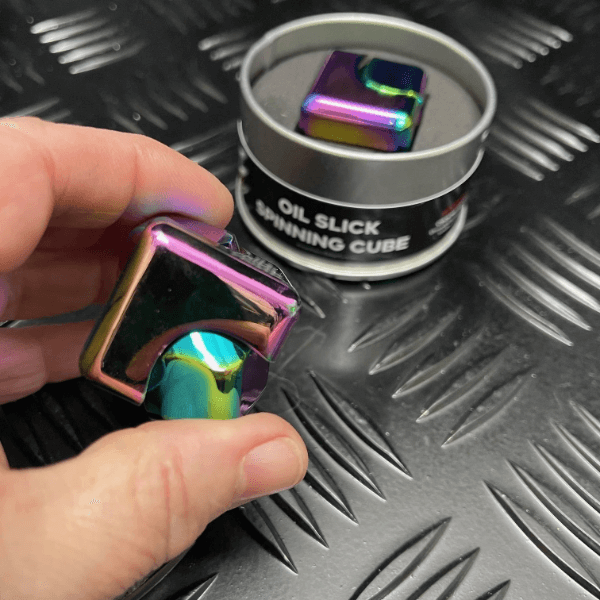 oil slick metal spinning cube shown in tin and one being held between 2 fingers-fun fidgets